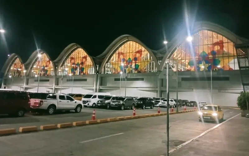 Mactan-Cebu International Airport Terminal 2 at dusk, its sweeping timber-arched roof lit, with transfer vehicles waiting outside