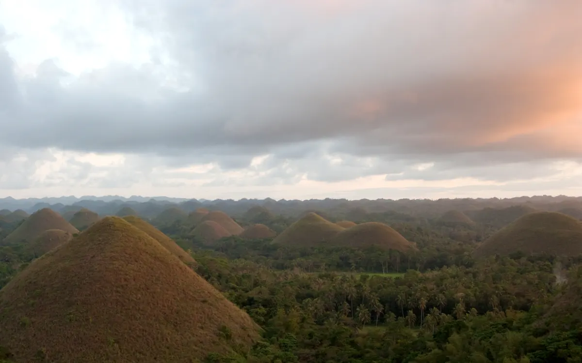 The Chocolate Hills of Bohol at sunset, rows of green cone-shaped hills fading into the distance