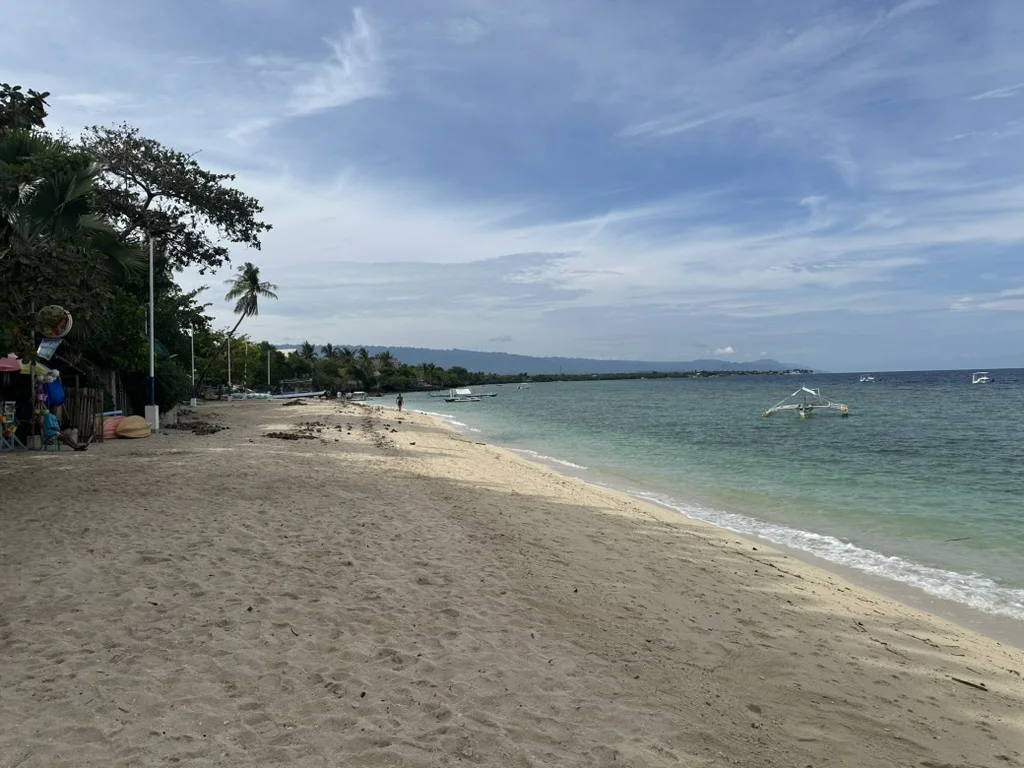 An outrigger boat anchored off the pale sand and clear turquoise water of White Beach (Basdako), Moalboal, Cebu